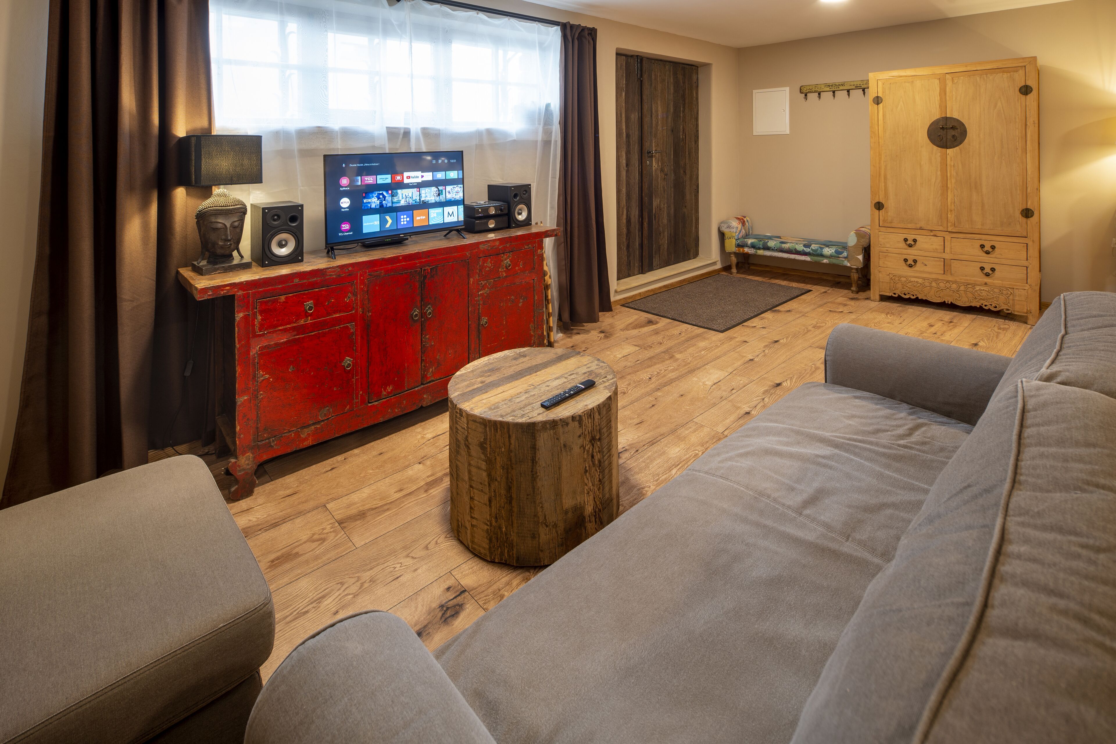 Una sala de estar con un aparador rojo, una mesa de centro de madera, un sofá gris y un televisor sobre un mueble de madera.