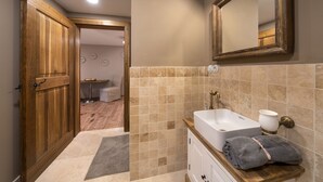 A bathroom with a wooden door, beige tiles, a white sink, and a towel on the counter.