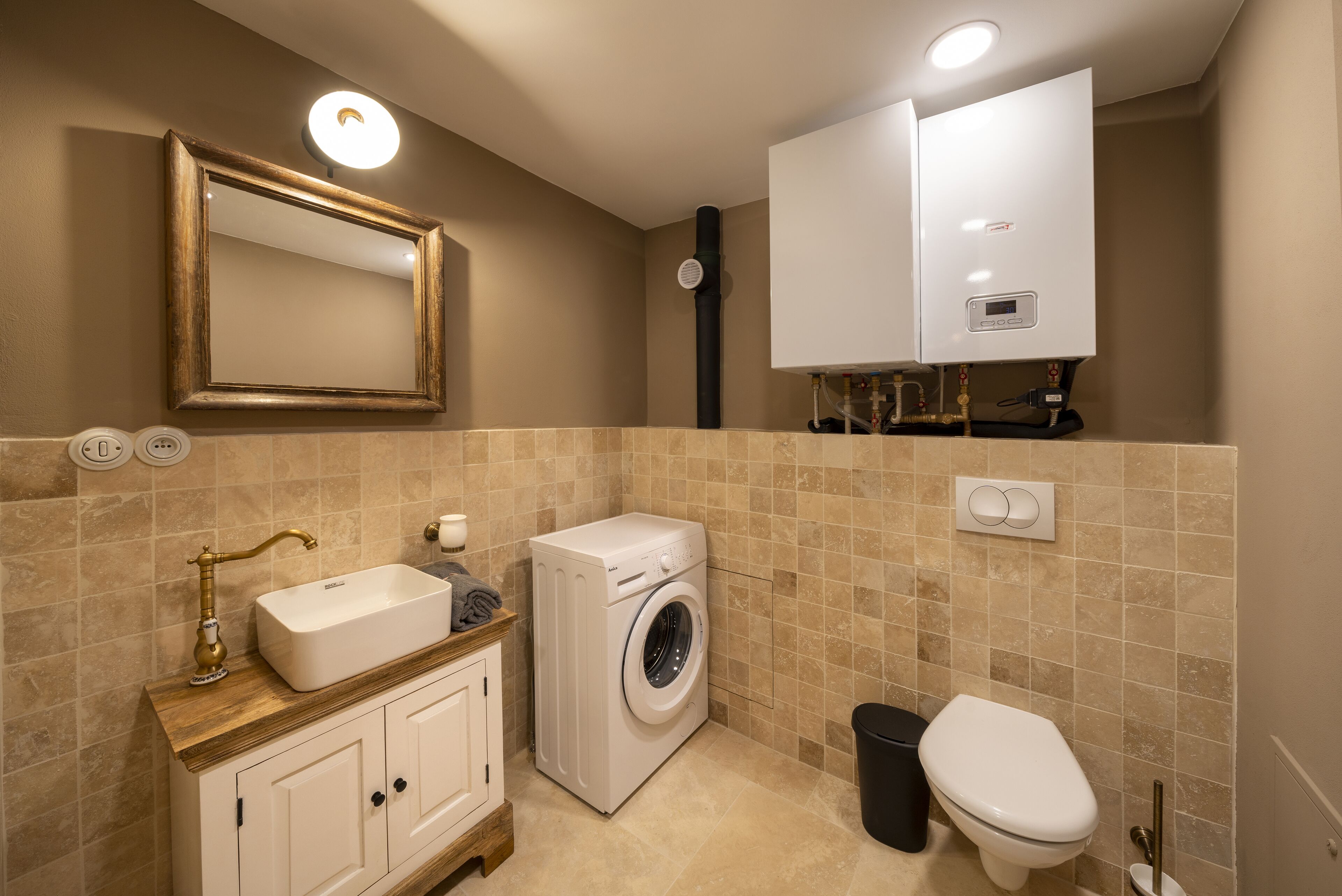A bathroom with a sink, mirror, washing machine, toilet, and a cabinet.