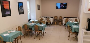 Zona pranzo con tavoli e sedie, una televisione appesa al muro e quadri incorniciati.