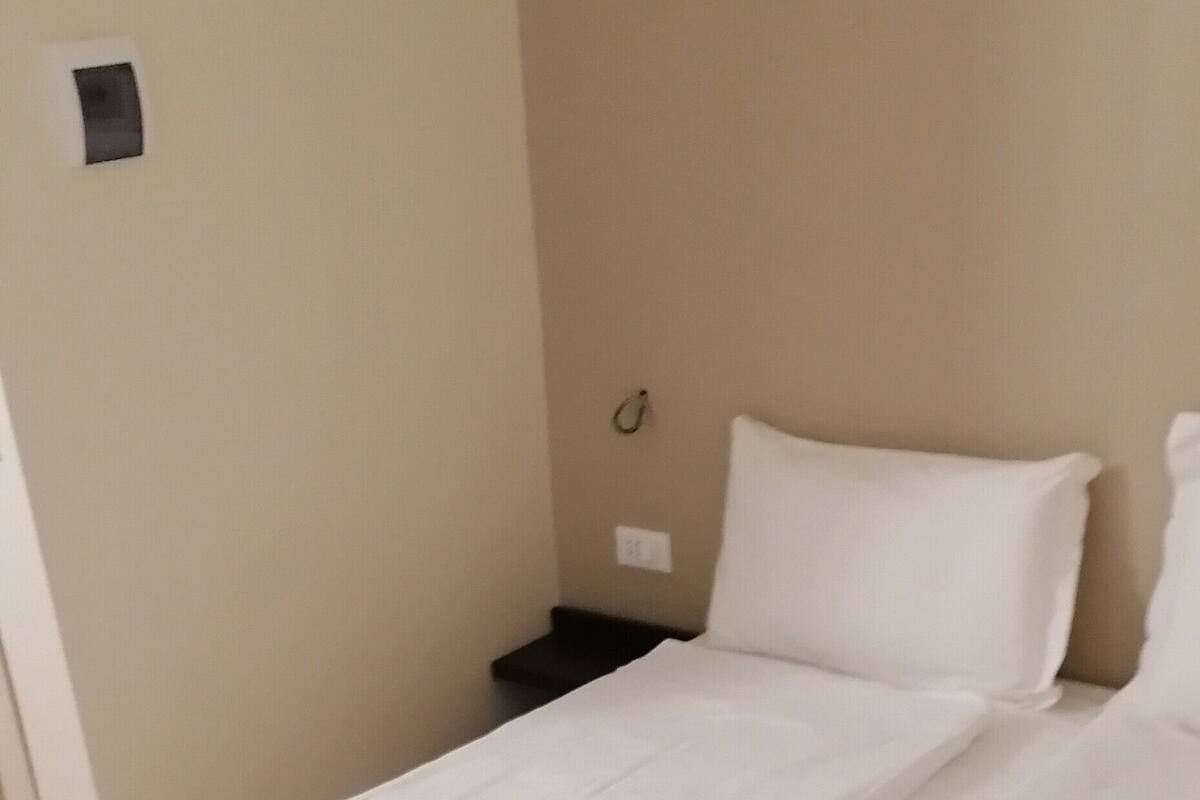 A single-bed room with a wooden floor, white bedding, and a small bedside table.