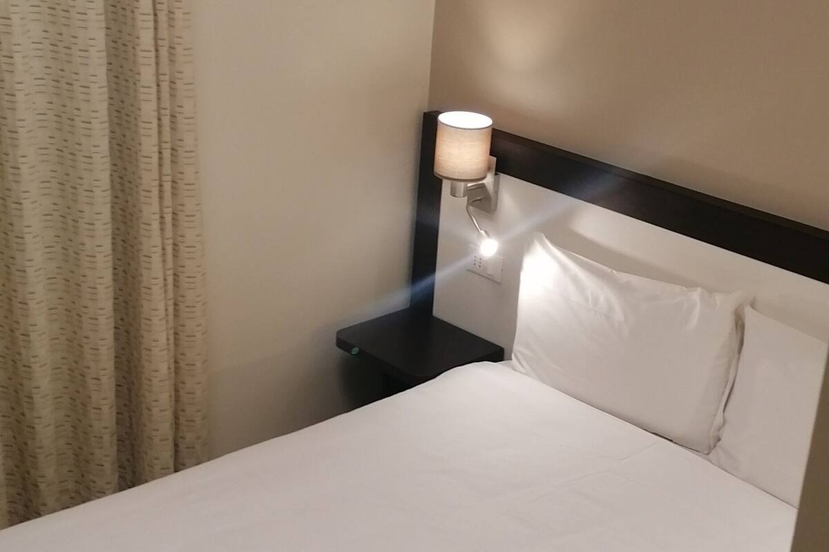 A hotel room with a bed, a nightstand with a lamp, and a curtain.