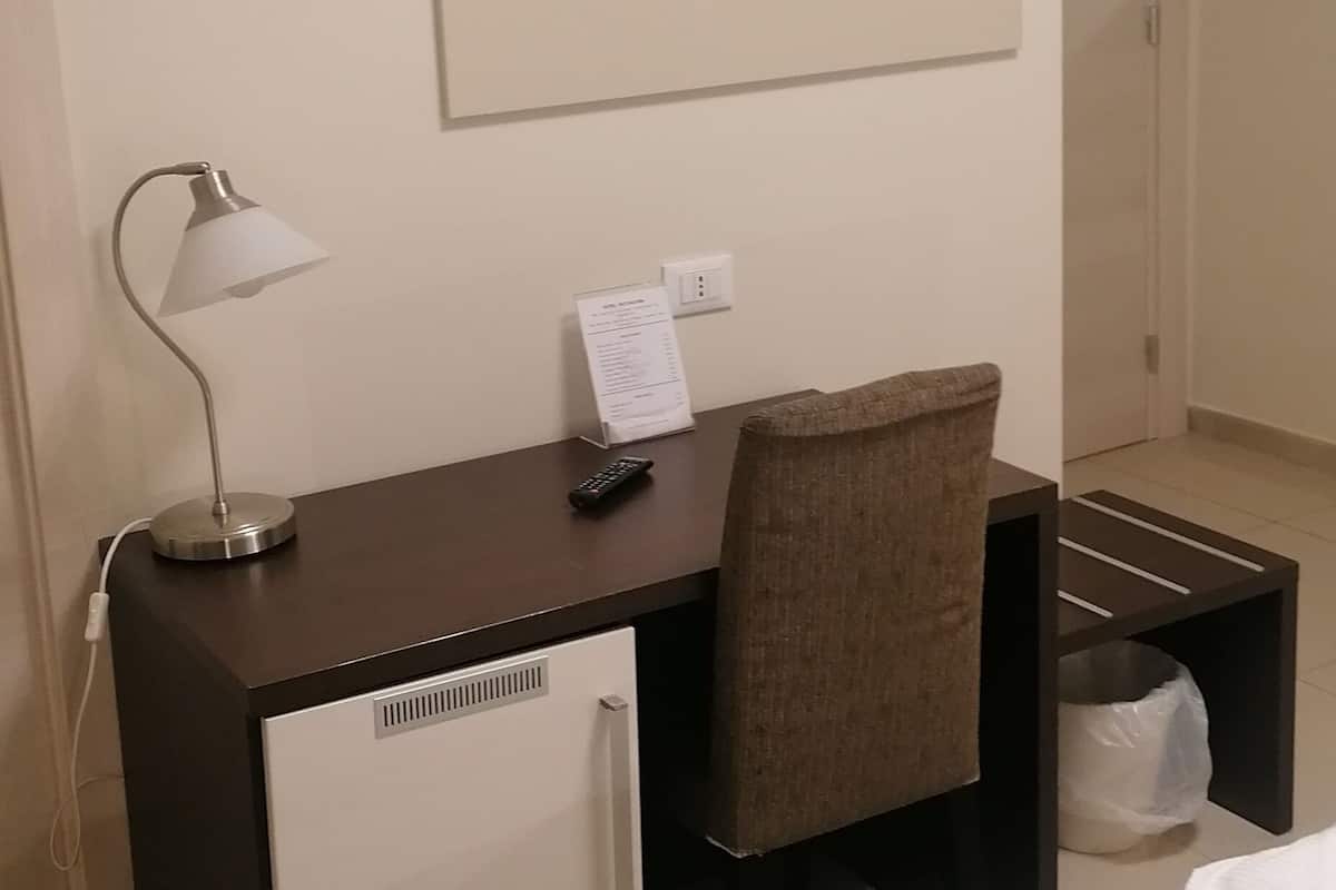 A hotel room with a bed, a desk with a lamp, a TV mounted on the wall, and a small cabinet.
