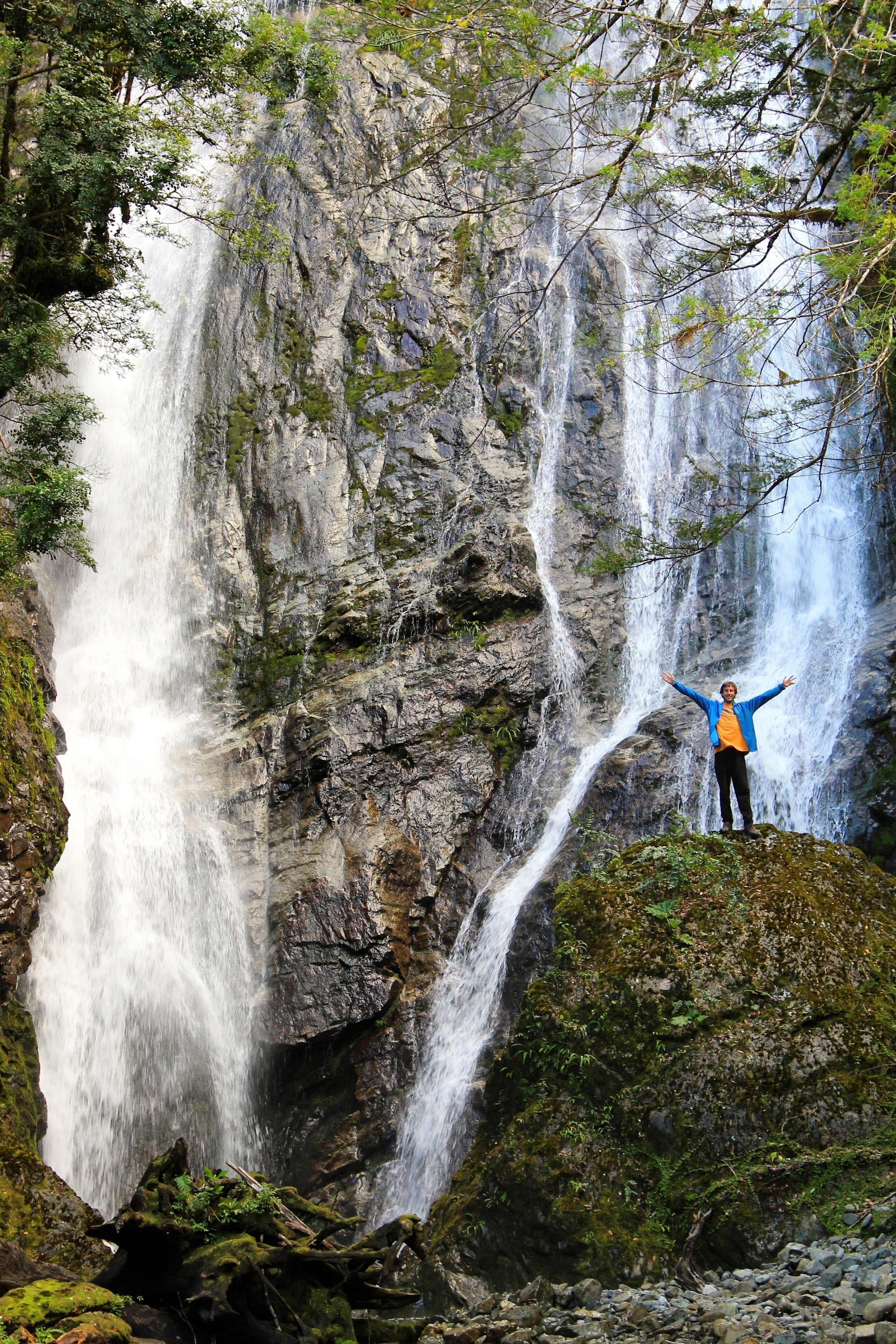 Une cascade, avec une personne debout sur un rocher, les bras tendus.