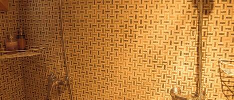 A bathroom with patterned tile walls, a shower with a handheld showerhead, and a small shelf with toiletries.