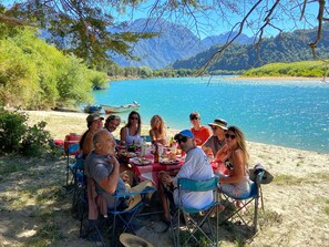 Un groupe de personnes est réuni autour d’une table en plein air, avec un lac et des montagnes en arrière-plan.