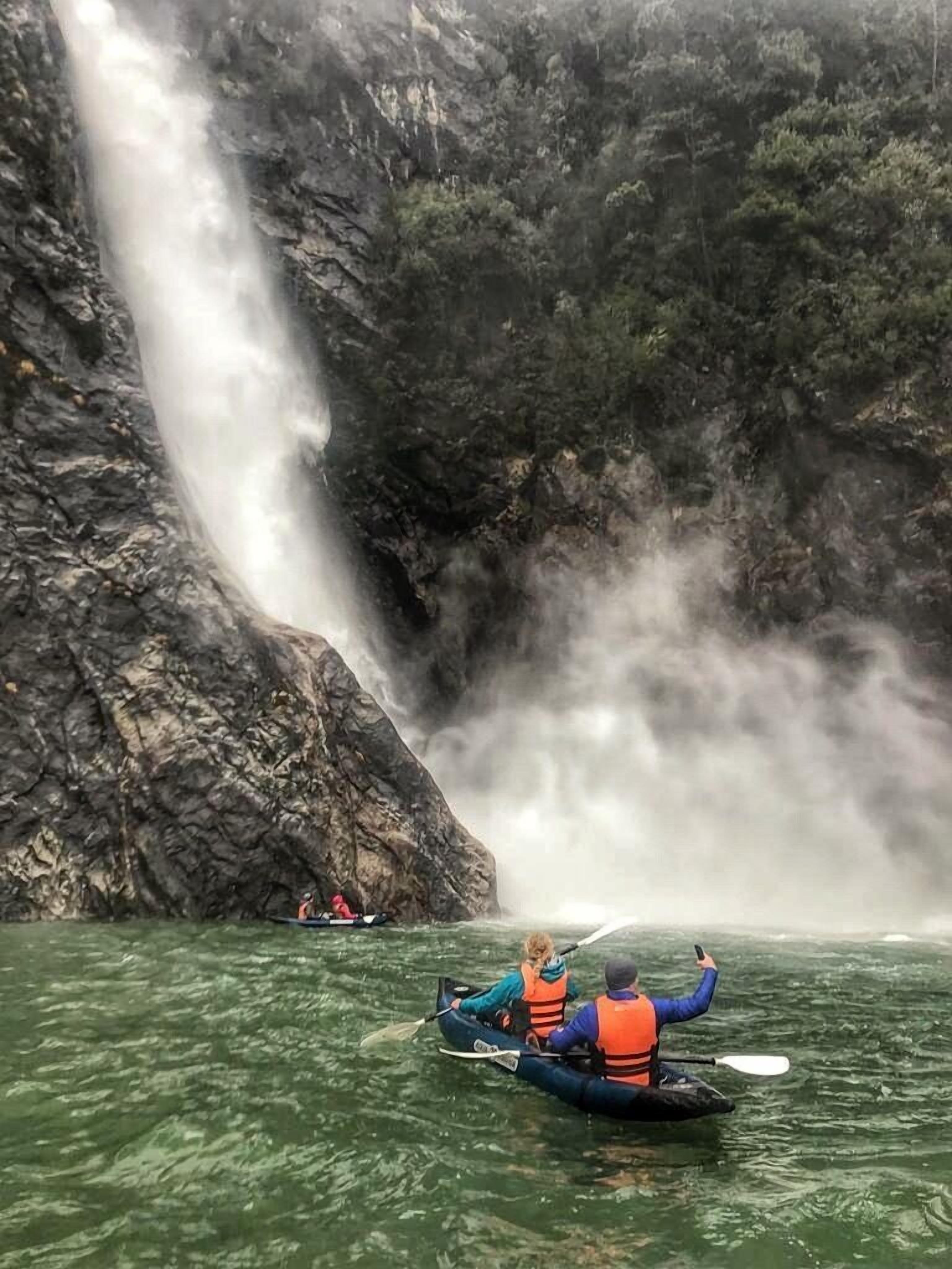 Un grupo de personas haciendo kayak en un río, con una cascada al fondo.