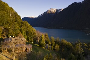 Un chalet de montagne doté de panneaux solaires, entouré d’une forêt dense et situé près d’un lac.