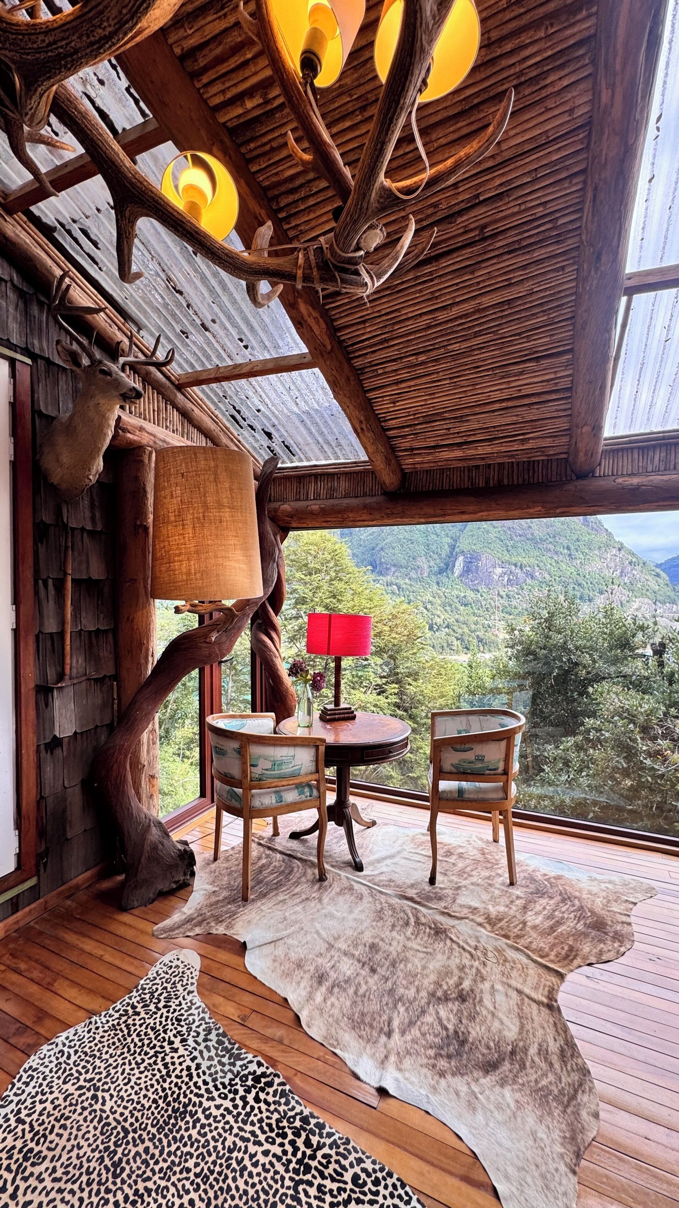 Un intérieur rustique avec un plafond en bois, une table entourée de chaises, un tapis en fourrure et une décoration représentant une tête de cerf.