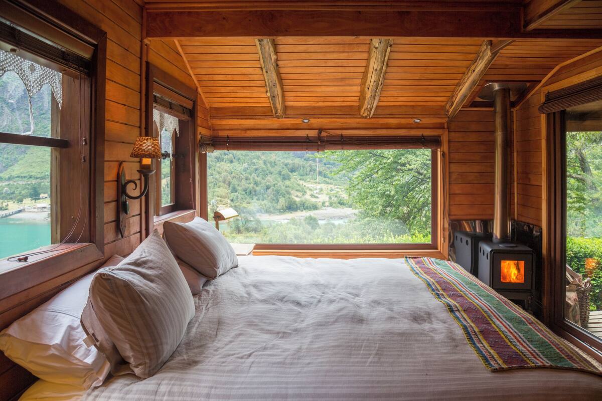 Quarto de cabana de madeira com uma cama, uma janela com vista para uma floresta e uma lareira a lenha.