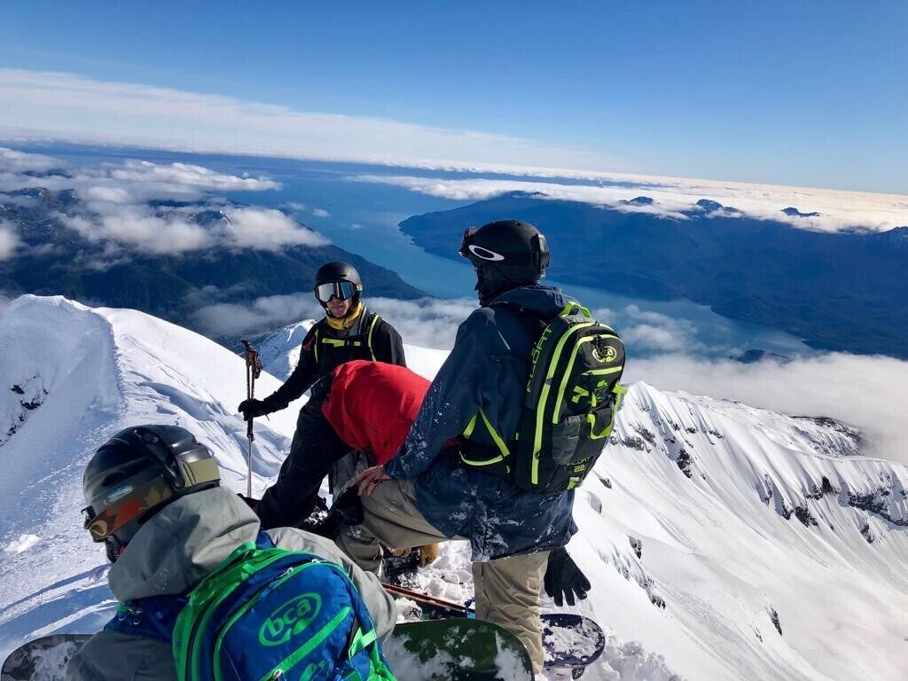 A group of people on a snowy mountain peak with a clear view of the sky and clouds below.