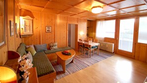 A wooden cabin interior with a sofa, dining table, chairs, and a radiator. - Cosy Retreat Apartment -Top 39 (Kaprun)