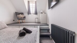 A bedroom with a bed, a chair, a desk, a radiator, and a window. - Castle Garden View - Two Steps from Central Rochester High Street (Rochester)
