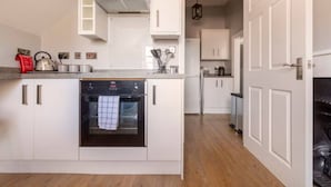 A compact kitchen with white cabinets, a built-in oven, and a stainless steel kettle on the countertop. - Castle Garden View - Two Steps from Central Rochester High Street (Rochester)