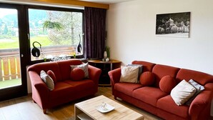 A living room with two red sofas, a wooden coffee table, and a view through a glass door. - Apartment Zachary (Kaprun)