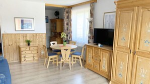 A cozy room with wooden furniture, a dining table, chairs, a cabinet, and a television.