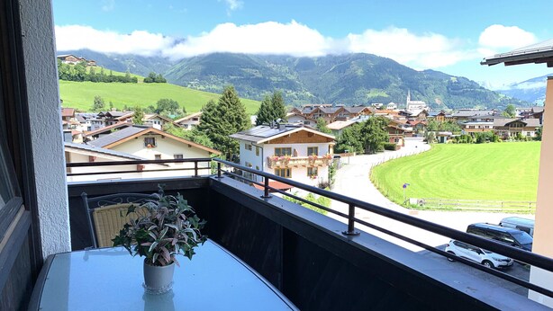 A balcony with a view of a residential area, including houses and a green field.