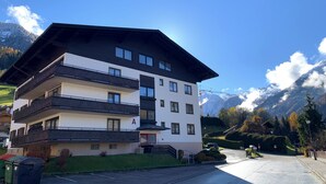 A multi-story hotel with balconies, a parking area, and a mountainous backdrop. - Panorama Deluxe Studio-Top 12 (Kaprun)