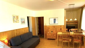 A room with a bed, a sofa, a dining table with chairs, wooden walls, and a ceiling light fixture. - Panorama Deluxe Studio-Top 12 (Kaprun)