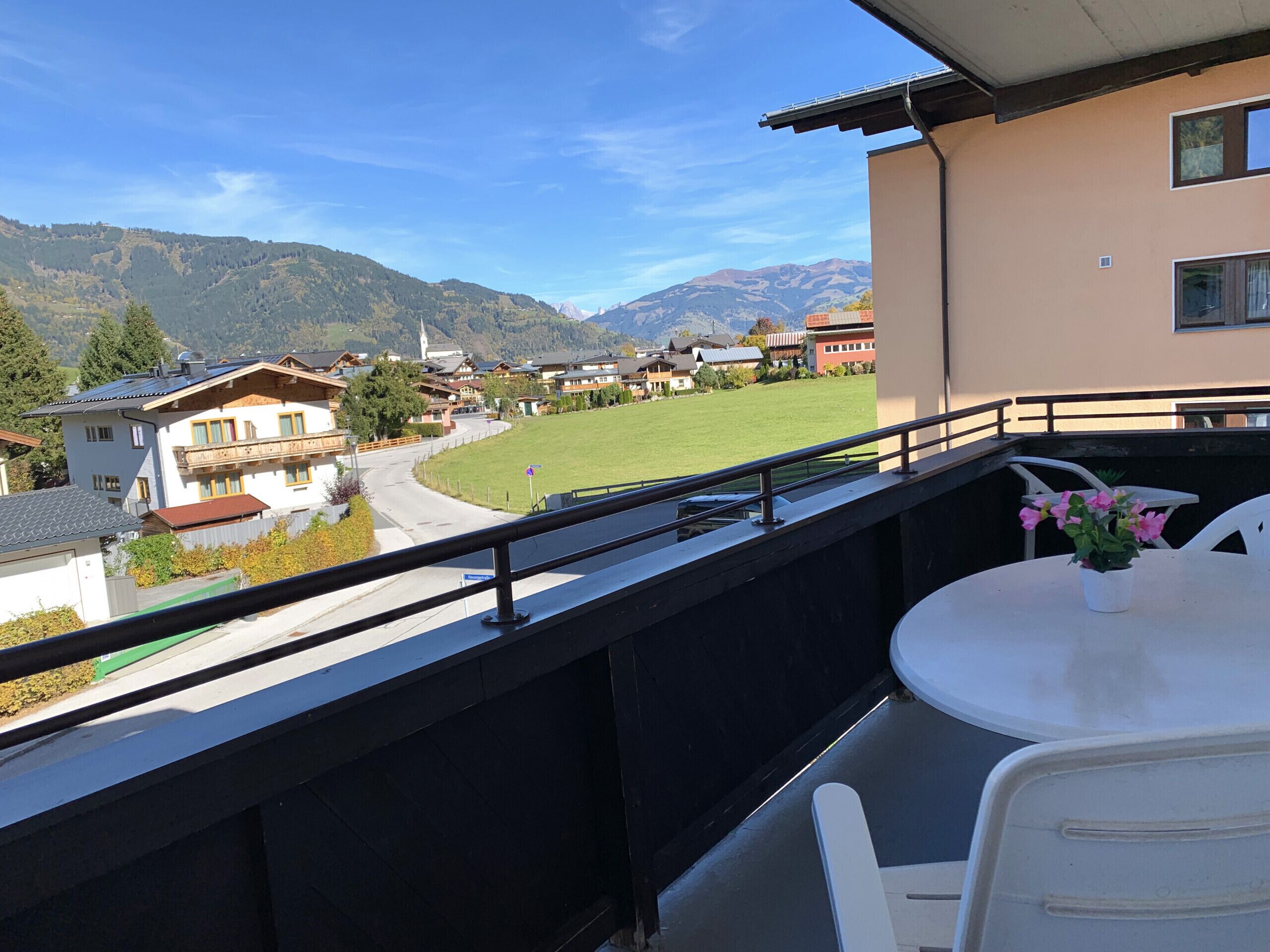 A balcony with a view of a village, a grassy field, and mountains in the distance.