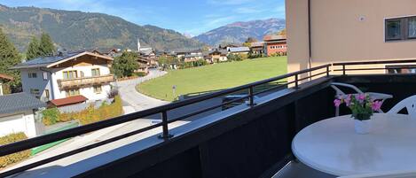A balcony with a view of a village, a grassy field, and mountains in the distance.