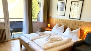 A hotel room with a wooden bed, two pillows, a bedside table with a lamp, and a view of the outdoors. - Panorama Deluxe Studio-Top 12 (Kaprun)
