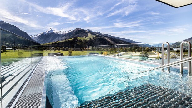 A swimming pool with clear blue water, surrounded by a metal deck and glass panels, offering a view of snow-capped mountains and a clear sky. - Panorama Deluxe Studio-Top 12 (Kaprun)