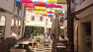 A courtyard with colorful umbrellas hanging overhead, tables and chairs, and a building with a sign reading "CELLA CENTRAL". - Panorama Deluxe Studio-Top 12 (Kaprun)