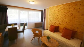 Ein Wohnzimmer mit Backsteinwand, einer Couch mit orangefarbenen Kissen, einem Esstisch mit Stühlen und einem Korbstuhl.