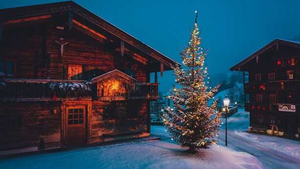 Ein rustikales Holzgebäude mit verschneitem Grund und einem geschmückten Weihnachtsbaum.