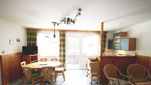 A dining area with a wooden table and chairs, a television, and a kitchen area with cabinets and a counter.