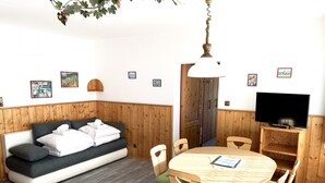 A cozy room with a wooden panel wall, a sofa with white towels, a round wooden table with chairs, and a TV on a wooden stand.