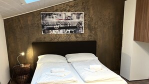A modern bedroom with a skylight, a bed with white linens, a headboard, a wall-mounted artwork, and a small side table.