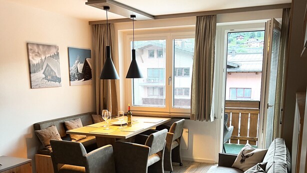 A cozy living room with a sofa, a dining table with chairs, a coffee table, and a rug. There are two pendant lights above the table.