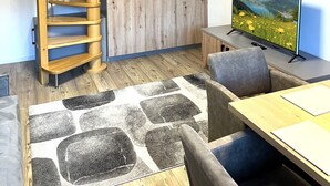 A modern interior with a wooden spiral staircase, a flat-screen TV, and a dining area with a patterned rug.
