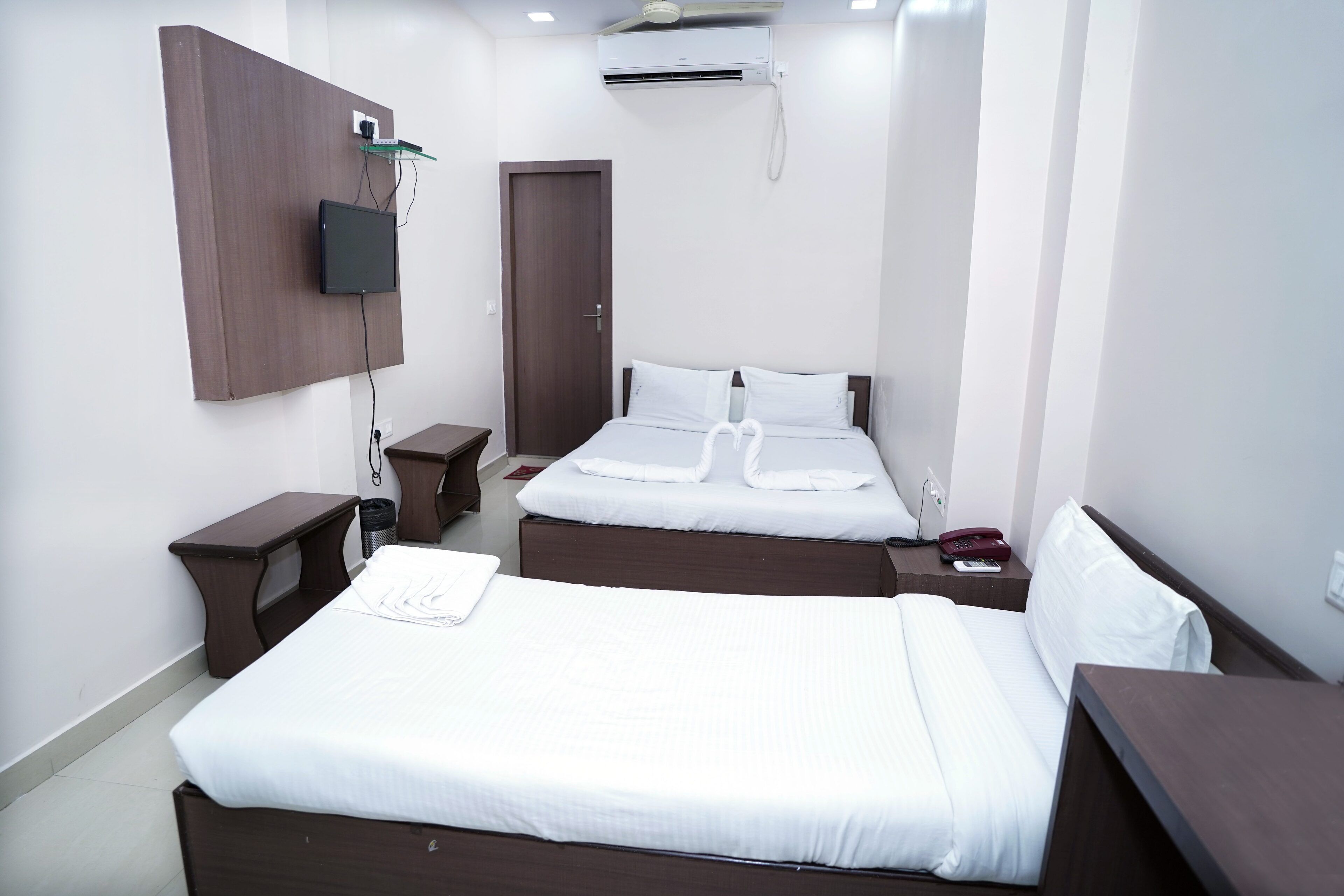 A hotel room with two beds, a TV mounted on the wall, a bedside table, and a small desk.