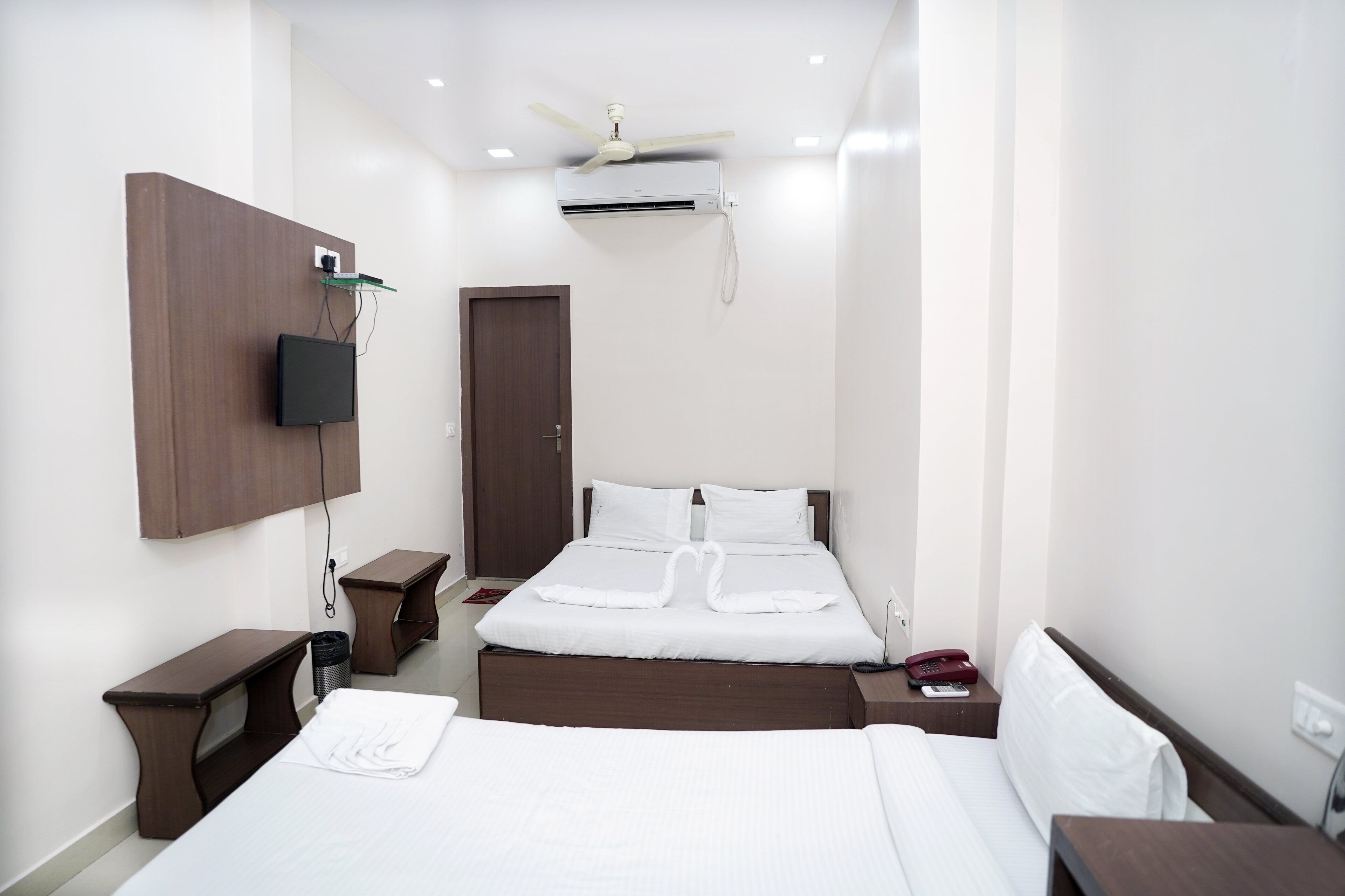 A hotel room with two beds, a TV mounted on the wall, a ceiling fan, and an air conditioning unit.