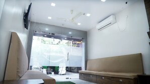 A modern room with a sofa, a wooden bench, a ceiling fan, and an air conditioning unit. - Sonar Bangla Guest House (Kolkata)