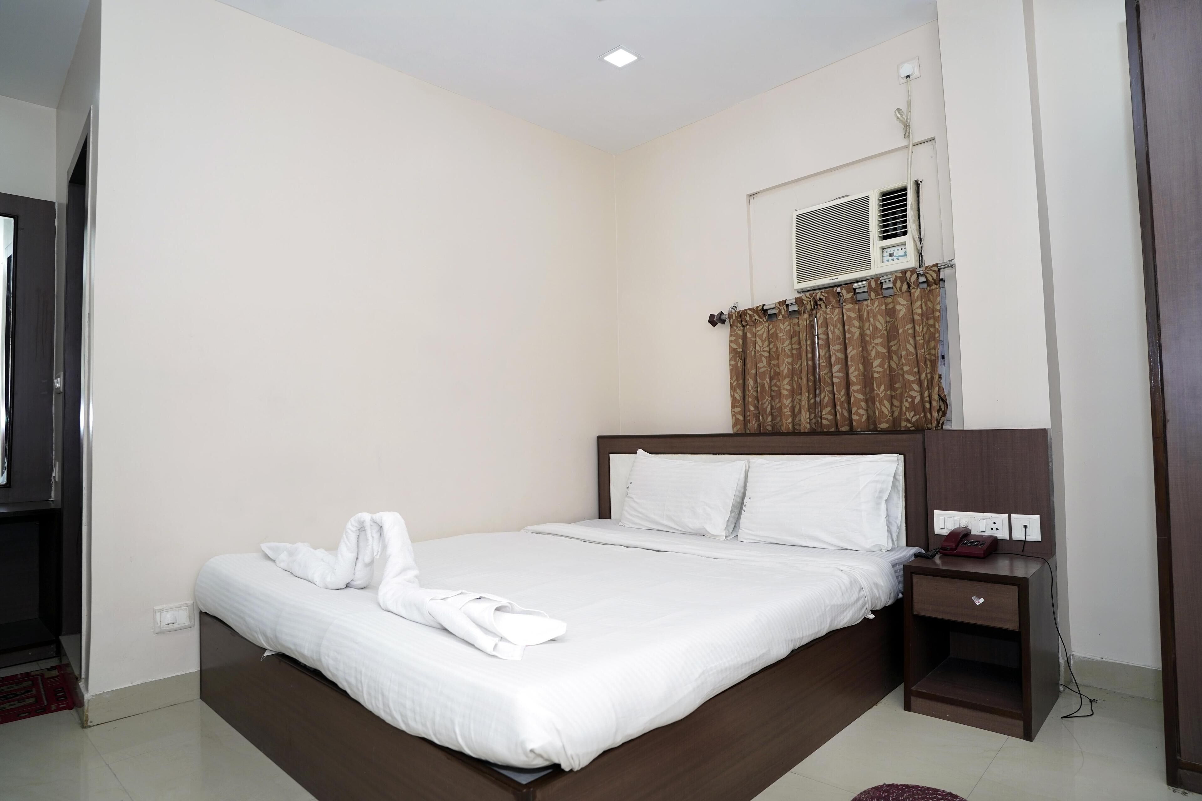 A hotel room with a large bed, a bedside table, an air conditioning unit, and a curtain.