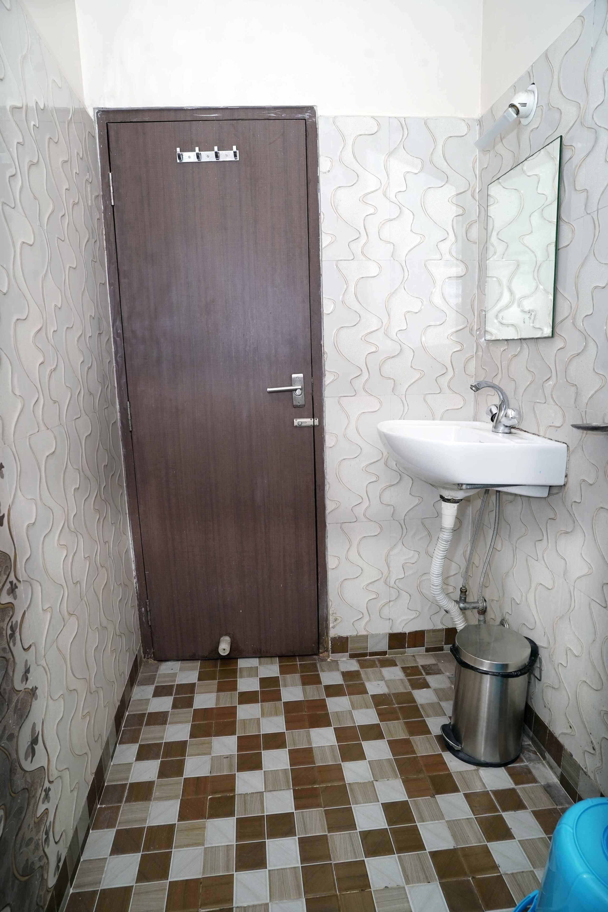 Un baño con una puerta marrón, un lavamanos blanco, un cubo de basura y paredes con diseño.