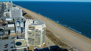 An aerial view of a coastal city with a prominent hotel featuring a circular rooftop and a parking lot. - Beautiful sunset and ocean view from 2 Bedroom Condo with Free WiFi and an Outdoor Pool Located in Midtown Only Steps to Beach! (Ocean City)
