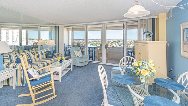 A spacious living area with a sofa, chairs, a dining table, and a balcony with a view. - Beautiful sunset and ocean view from 2 Bedroom Condo with Free WiFi and an Outdoor Pool Located in Midtown Only Steps to Beach! (Ocean City)