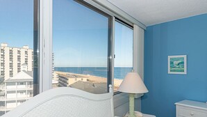 A bedroom with a large window offering a view of the beach and buildings. - Beautiful sunset and ocean view from 2 Bedroom Condo with Free WiFi and an Outdoor Pool Located in Midtown Only Steps to Beach! (Ocean City)