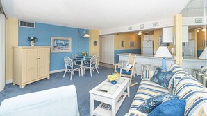 A compact living space with a dining area, kitchenette, and a sofa with striped cushions. - Beautiful sunset and ocean view from 2 Bedroom Condo with Free WiFi and an Outdoor Pool Located in Midtown Only Steps to Beach! (Ocean City)