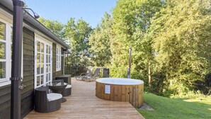 Eine Holzterrasse mit Sitzgelegenheiten im Freien, einem Whirlpool und einem Haus mit großen Fenstern.