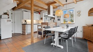 Eine moderne Küche mit weißen Schränken, ein Essbereich mit weißem Tisch und Stühlen und ein großes Fenster mit Blick auf Bäume.