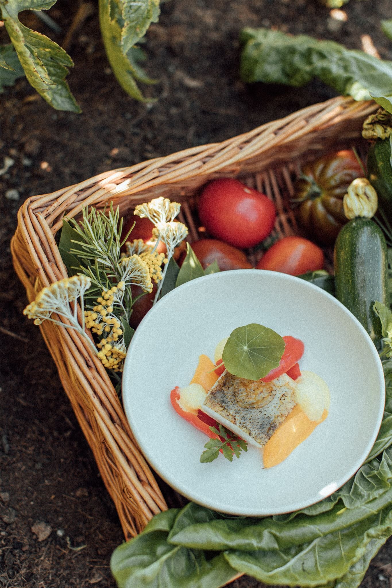 A wicker basket filled with fresh vegetables and a plate of food.
