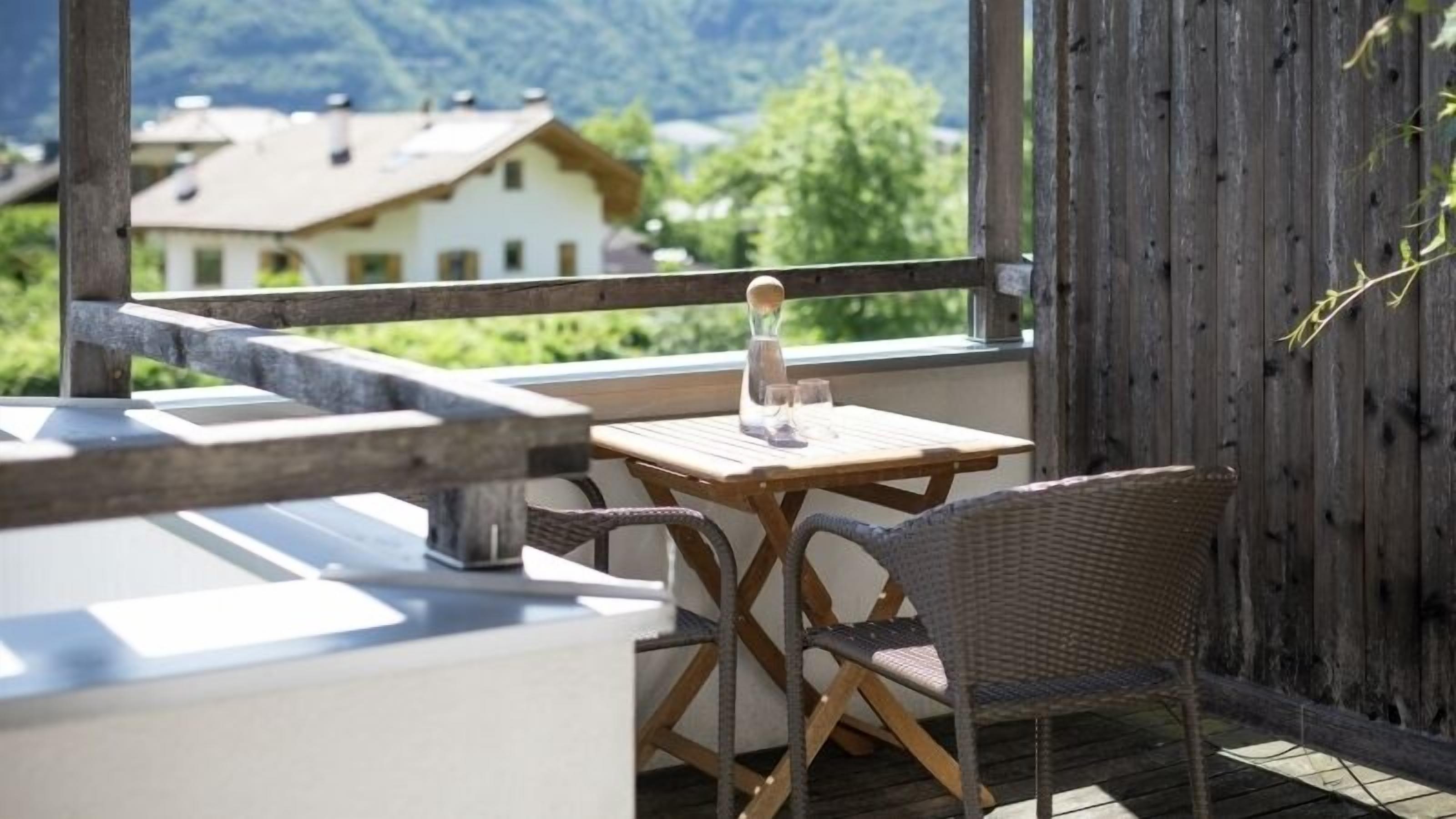 A wooden deck with a table and chairs, overlooking a mountain and a house.