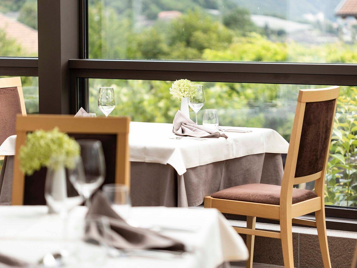 A dining area with a table set for two, a chair, and a window with a view of greenery.