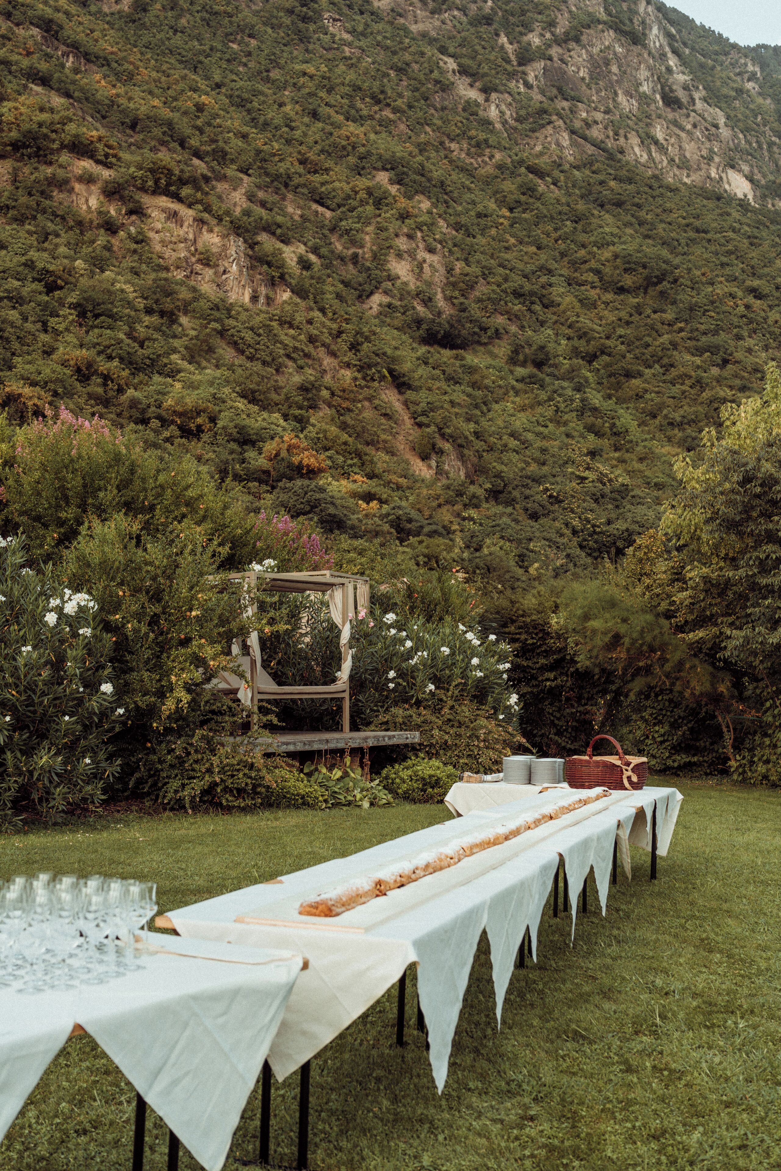 Mesa comprida montada ao ar livre, com toldo, cercada por vegetação exuberante e montanhas ao fundo.